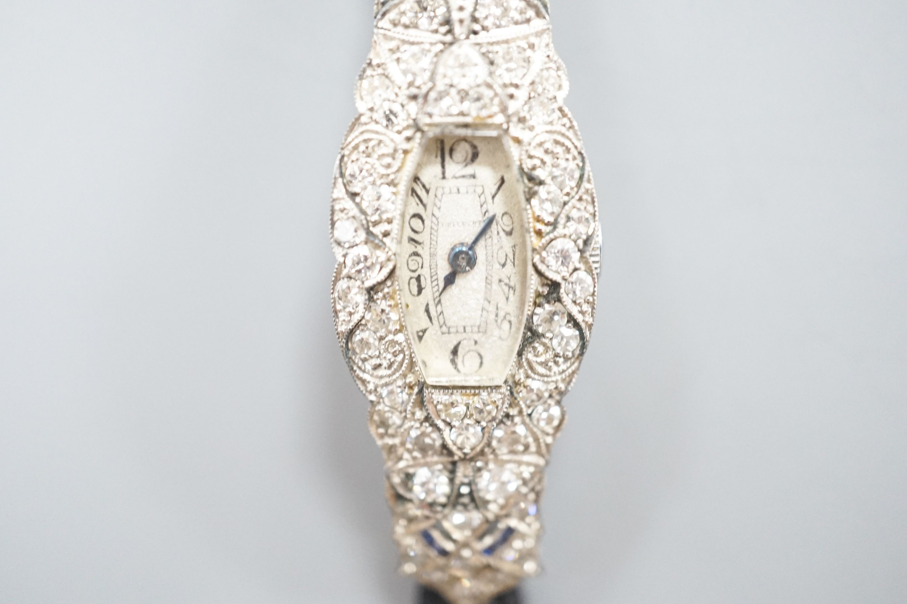 A lady's mid 20th century engraved white metal, diamond and sapphire set cocktail watch, case diameter 17mm, gross weight 18.3 grams, on a later? twin strand fabric strap.